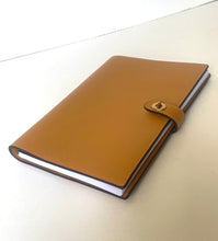 Load image into Gallery viewer, A tan leather planner or notebook cover with a snap-button strap closure, shown closed on a plain light background.