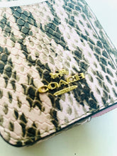 Load image into Gallery viewer, Close-up of a Coach handbag featuring a snakeskin pattern in beige, black, and gray, with a gold-tone metal logo plaque on the front.