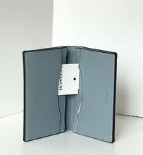 Load image into Gallery viewer, A Coach slim bifold card holder in textured light blue leather, shown open with a white brand tag attached, set against a clean white background.