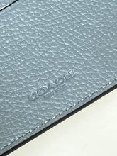 Load image into Gallery viewer, Close-up of a Coach New York pebbled leather item in a muted blue-gray color, showing the textured leather grain and debossed logo.