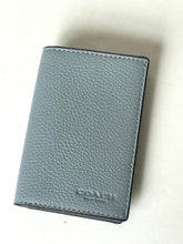 Load image into Gallery viewer, A Coach leather card holder wallet in a muted blue-gray color with a pebbled texture, featuring the debossed 'COACH NEW YORK' logo near the bottom right corner.