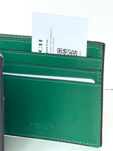Load image into Gallery viewer, A green leather Coach cardholder wallet with a white business card partially inserted into the card slots, photographed against a clean white background.