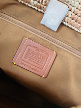 Load image into Gallery viewer, Close-up of a Coach bag interior showing a tan leather brand patch with yellow stitching, a brown nylon body, a zipper, and part of a woven straw-like top surface.
