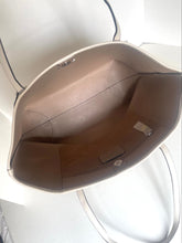 Load image into Gallery viewer, An overhead view of a light beige tote bag showing its interior lining and silver-tone hardware.