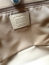 Load image into Gallery viewer, Close-up of a Coach handbag interior showing a metallic silver brand patch on a taupe-beige nylon fabric, with a zipper running horizontally.