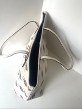Load image into Gallery viewer, A cream-colored canvas tote bag with a delicate multicolor feather print, featuring a dark navy blue interior lining and a thin dark trim along the edges, shown leaning against a white wall.