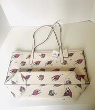 Load image into Gallery viewer, An off-white tote bag with a colorful cartoon dog print, shown with its matching zippered pouch and shoulder straps on a white surface.