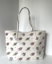 Load image into Gallery viewer, An off-white tote bag with a repeating pattern of cartoonish flying creatures in purple, pink, and green, featuring light gray shoulder straps, set against a plain light gray background.