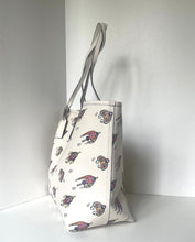 Load image into Gallery viewer, An off-white canvas tote bag with a repeating pattern of cartoon dogs wearing sunglasses, standing in a white corner.