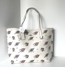 Load image into Gallery viewer, A white leather tote bag with an all-over print of cartoon dogs wearing sunglasses, featuring light gray leather handles and a hanging white brand tag.