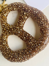 Load image into Gallery viewer, Gold glittery pretzel-shaped object on a white background
