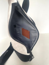 Load image into Gallery viewer, Close-up of an open shoulder bag showing the interior lining, zipper, and a brown leather brand patch inside. The exterior has a light beige and white monogram pattern with black trim and strap.