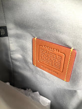 Load image into Gallery viewer, Close-up of a Coach leather luggage tag attached to a gray textured fabric bag, with visible yellow stitching and the Coach logo embossed on the tag.