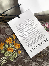 Load image into Gallery viewer, Coach handbag with floral embroidery and a product information card.