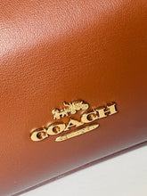Load image into Gallery viewer, Close-up of a brown leather Coach bag with gold logo.