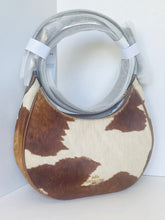 Load image into Gallery viewer, A brown and cream cowhide shoulder bag with a silver zipper and a wrapped silver handle, shown on a plain white background.