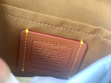 Load image into Gallery viewer, Close-up of a Coach bag's interior lining, showing a brown leather brand patch with embossed text and gold contrast stitching on a tan canvas background.