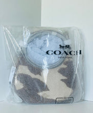 Load image into Gallery viewer, A Coach New York branded clear plastic bag containing a plush circular throw pillow. The pillow features a beige and dark brown abstract pattern, with a light blue-gray circular inset in the center.