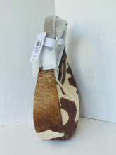 Load image into Gallery viewer, A small shoulder bag with a brown and cream cowhide pattern, featuring a light beige fabric strap and a white paper tag attached, set against a plain white background.