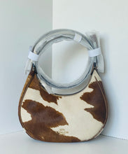 Load image into Gallery viewer, A Coach hobo shoulder bag in brown and cream cowhide, wrapped in protective plastic on the handle, set against a clean white corner background.