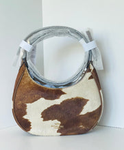 Load image into Gallery viewer, A Coach hobo shoulder bag made of brown and cream cowhide, featuring a silver-tone metal handle wrapped in protective plastic and white shipping bands.