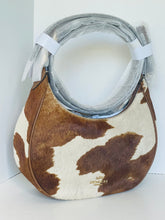 Load image into Gallery viewer, A Coach shoulder bag in brown and white cowhide, featuring a silver-tone metal ring handle and a small gold Coach logo near the bottom right, photographed against a plain white background.