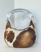 Load image into Gallery viewer, A small hobo handbag with a brown and cream cowhide pattern, featuring a circular silver-tone metal handle and white paper tags attached, set against a clean white background.