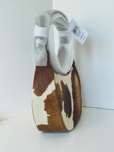 Load image into Gallery viewer, A small shoulder bag made from brown and cream cowhide, featuring a curved top handle wrapped in protective gray paper and a white product tag, set against a plain white background.