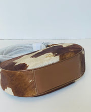 Load image into Gallery viewer, A small shoulder bag with a brown and white cowhide pattern top, a smooth brown leather side panel, and a gold-tone logo plaque on a white background.
