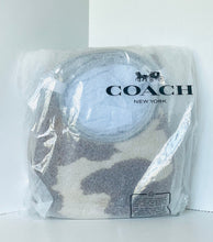 Load image into Gallery viewer, A Coach New York branded folded textile item wrapped in clear plastic packaging, showing a light gray and white patterned surface with the black COACH logo printed on the front.