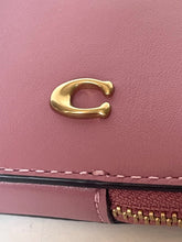 Load image into Gallery viewer, Close-up of a pink leather wallet or clutch featuring a polished gold-tone 'C' logo on the front flap and a matching zippered pocket with gold zipper teeth.