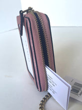 Load image into Gallery viewer, A pink textured leather zip-around wallet standing upright on a white surface, with a gold-tone zipper, black trim, and attached white product tags.