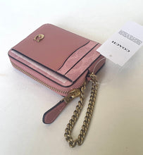 Load image into Gallery viewer, A Coach zip-around card holder wallet in dusty pink leather with a gold-tone horsebit logo, a gold-tone chain strap, and a white brand tag attached, set against a plain off-white background.