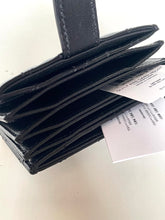 Load image into Gallery viewer, A black leather multi-card wallet with a strap closure, shown open with several cards partially inserted and a white product tag attached, photographed on a light neutral surface.