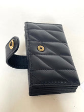 Load image into Gallery viewer, A black quilted leather wallet with a strap closure and gold-tone metal snap buttons, shown on a plain off-white background.