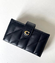 Load image into Gallery viewer, A black quilted leather wallet with a diagonal stitched pattern and a gold-tone 'C' logo clasp, photographed on a light off-white background.