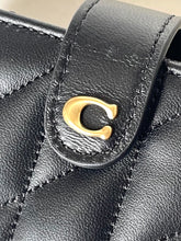 Load image into Gallery viewer, Close-up of a black quilted leather handbag featuring a prominent gold-tone 'C' logo clasp on a leather strap.