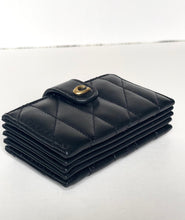Load image into Gallery viewer, A black quilted leather card holder wallet with a gold-tone snap button closure, displayed on a light gray surface.