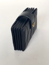 Load image into Gallery viewer, A black quilted leather bifold wallet with a gold-tone snap button closure, shown standing upright on a light gray surface.