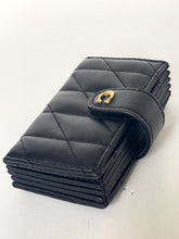 Load image into Gallery viewer, A black quilted leather wallet with a diagonal strap closure and a gold-tone metal snap button, shown on a plain off-white background.
