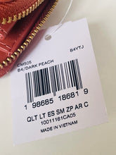 Load image into Gallery viewer, A close-up of a white retail hangtag attached to a dark peach leather zippered pouch, showing a barcode and printed text including 'CM505 B4/DARK PEACH' and 'MADE IN VIETNAM'.