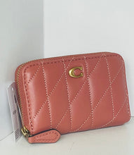 Load image into Gallery viewer, A Coach quilted zip-around wallet in dusty rose pink leather with a gold-tone C logo on the front, shown with its retail tag attached against a white background.