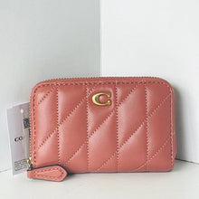 Load image into Gallery viewer, A pink quilted leather zip-around wallet with a gold-tone 'C' logo on the front, shown with a white hangtag against a white background.