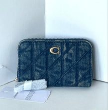 Load image into Gallery viewer, A dark blue quilted Coach zip-around wallet with a gold C logo, shown with its original paper tag and protective wrapping on a light gray surface against a white background.