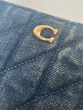 Load image into Gallery viewer, Close-up of a quilted blue denim bag featuring a gold-tone metal horseshoe charm.