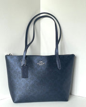 Load image into Gallery viewer, A dark navy blue Coach tote bag with a textured leather finish, featuring dual shoulder straps, a top zipper, and a silver-tone metal logo plate on the front.