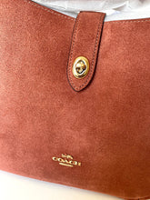 Load image into Gallery viewer, Close-up of a brown Coach handbag with a gold button and logo.