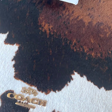Load image into Gallery viewer, Close-up of a Coach logo on a leather surface with brown and black color pattern.
