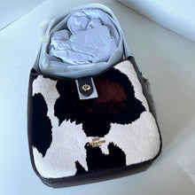 Load image into Gallery viewer, Cow print handbag with a visible brand logo on a light background