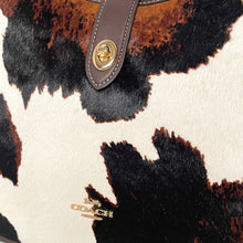 Load image into Gallery viewer, Close-up of a Coach handbag with cowhide pattern and gold logo.